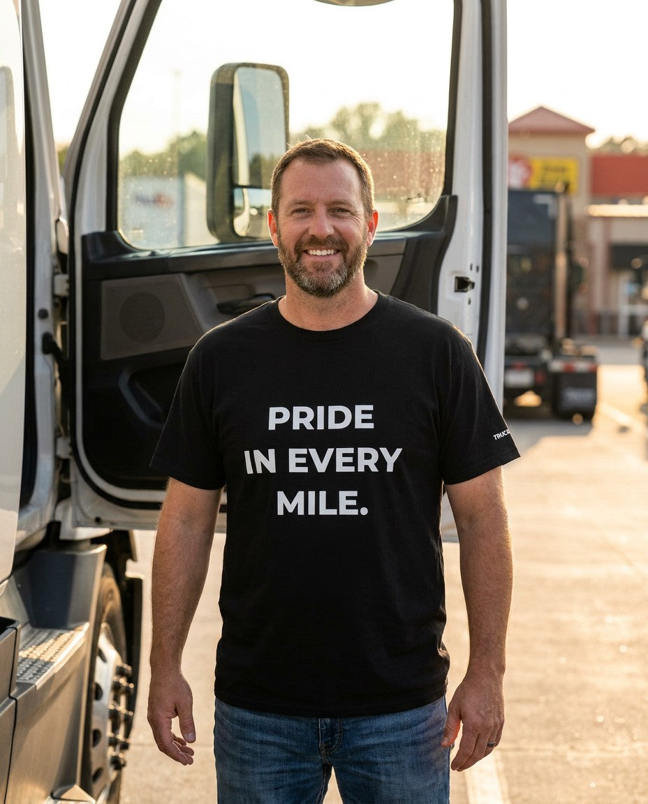 Pride in Every Mile Trucker Performance T-Shirt in black, worn by a truck driver beside his semi-truck