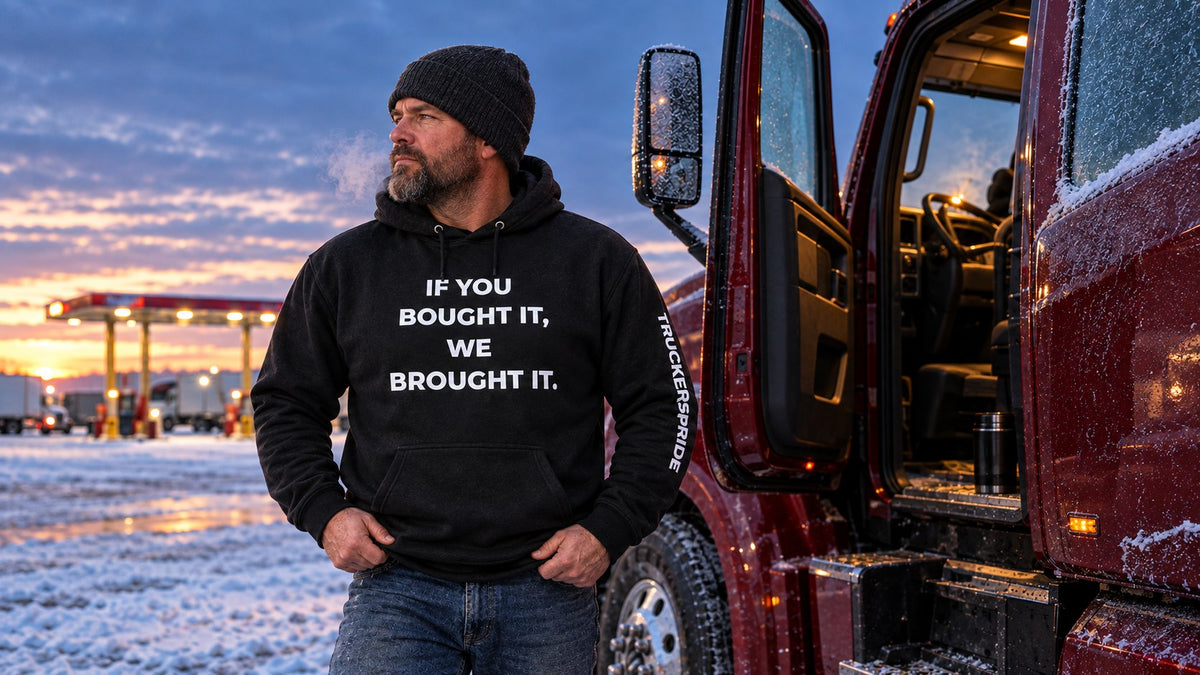 Truck driver in a black Trucker's Pride 'If You Bought It, We Brought It' hoodie beside his semi on a frosty winter morning